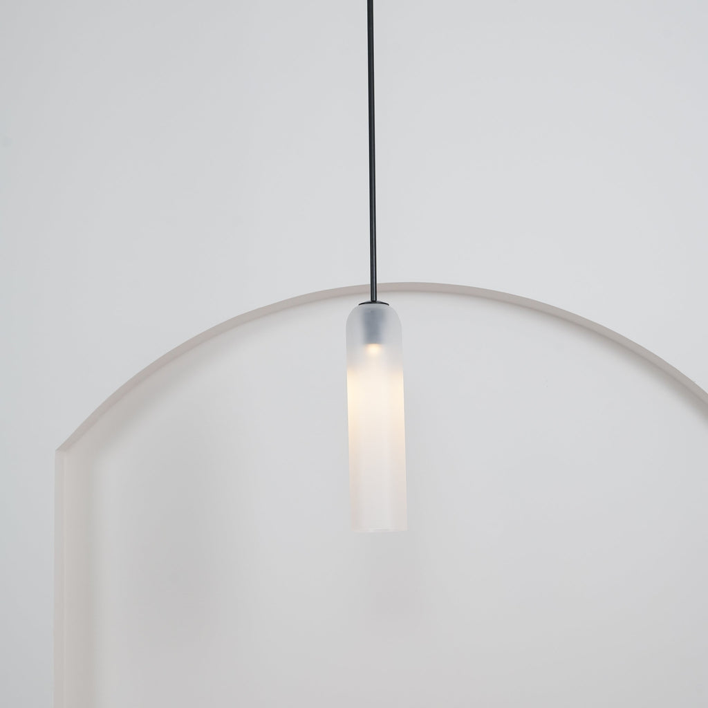 A tighter crop of the frosted white Clérachic pendant's black rod and shade glowing above the rounded archway.