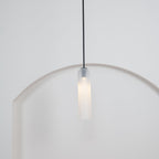 A tighter crop of the frosted white Clérachic pendant's black rod and shade glowing above the rounded archway.