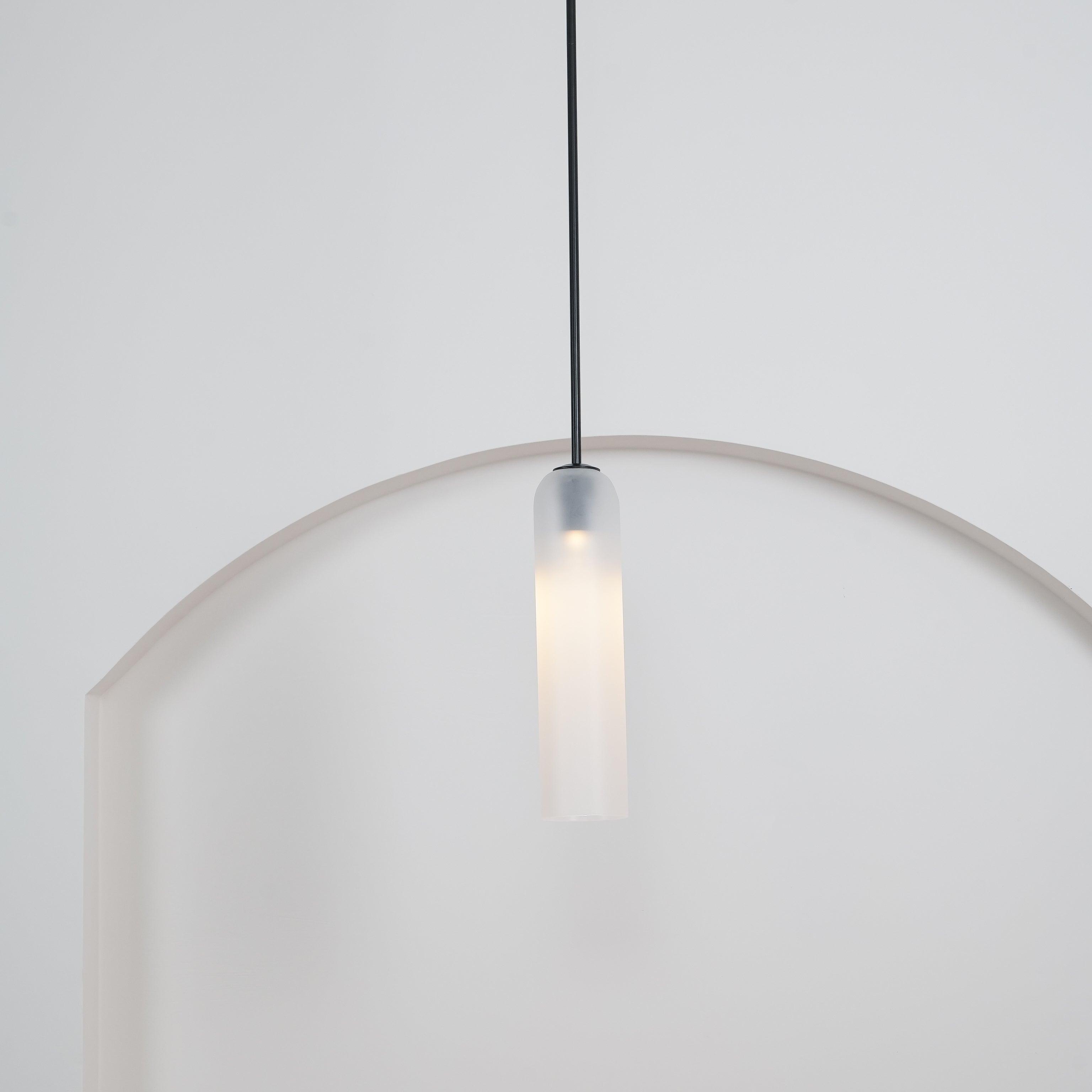 A tighter crop of the frosted white Clérachic pendant's black rod and shade glowing above the rounded archway.