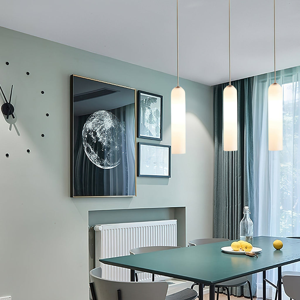 Three frosted white Clérachic pendants lit above a dining table, beside a wall clock and a framed moon photograph.