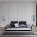 Two green Clérachic glass tube pendants flank a panelled headboard, lit above matching bedside cabinets.