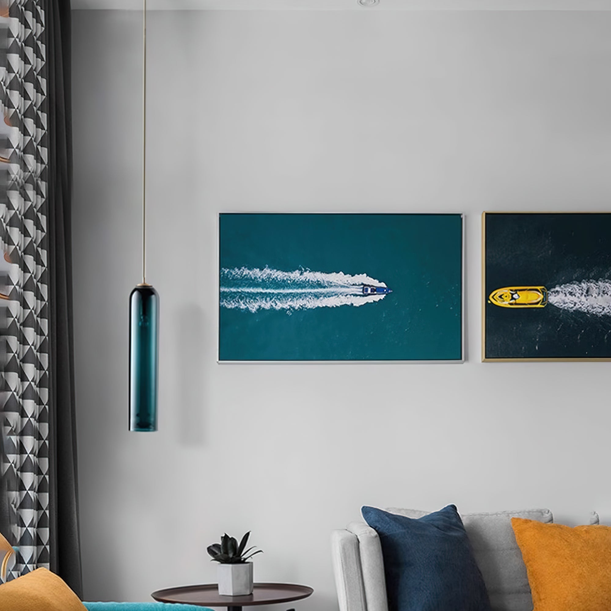 A green Clérachic glass tube pendant lit in a living room, beside framed aerial photography and a grey sofa.