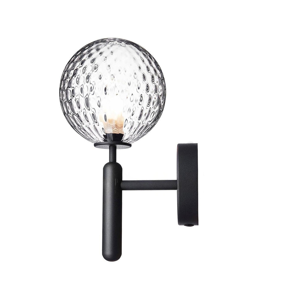 Unlit, this black Clérachic wall light shows its dimpled clear glass globe and angled arm against a plain white background.