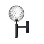 Unlit, this black Clérachic wall light shows its dimpled clear glass globe and angled arm against a plain white background.