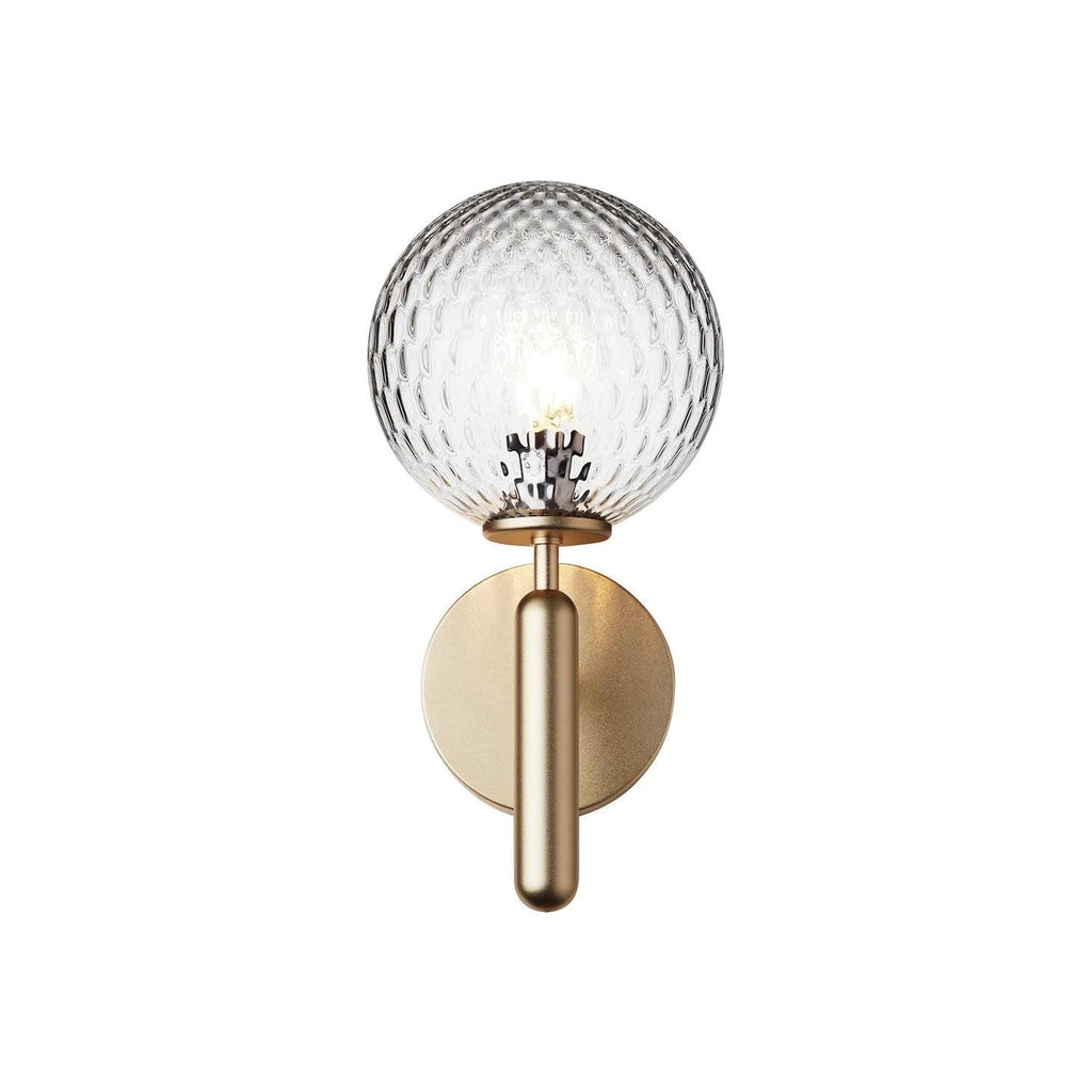 From another angle, this brass Clérachic wall light's lit dimpled clear glass globe shows against a plain white background.