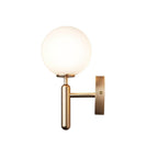 Unlit, this brass Clérachic wall light shows its round white glass globe against a plain white background.