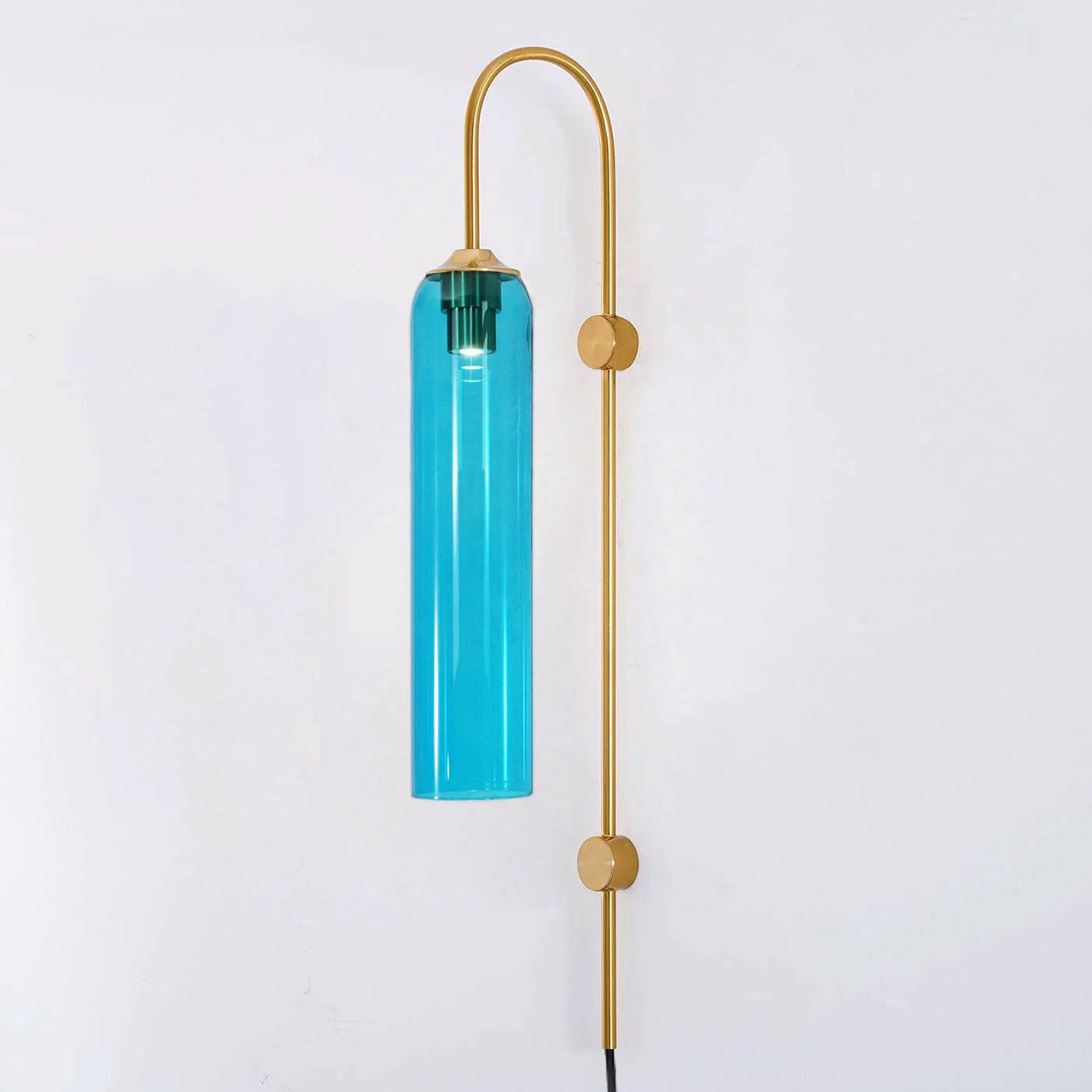 Sky blue glass on the Clérachic mouth-blown wall sconce with a gold body, lit and photographed against a plain white wall.