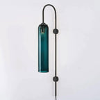 Deep teal glass on the black-bodied Clérachic mouth-blown wall sconce, shown unlit against a plain pale wall.