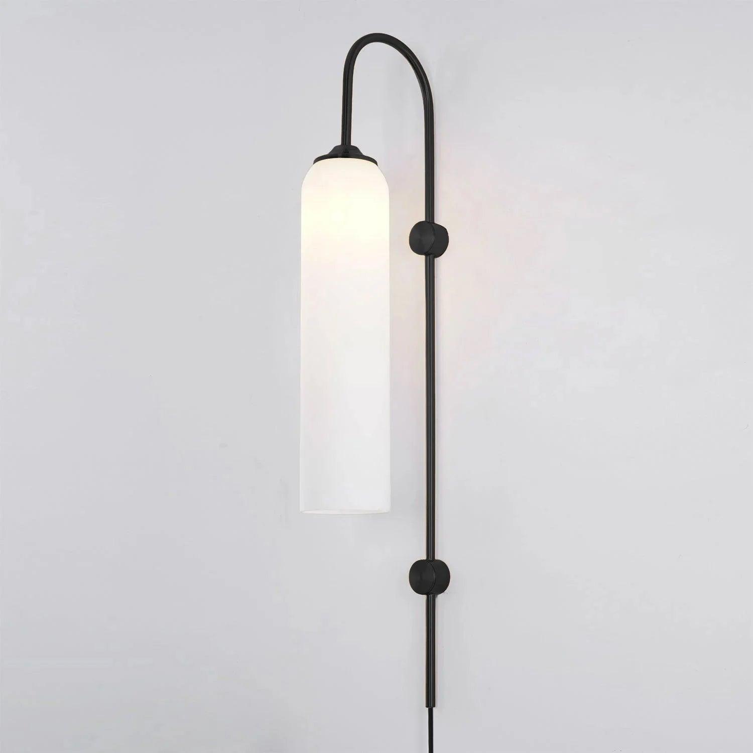 Milky white glass on the black Clérachic mouth-blown wall sconce, lit, with the cord dropping from the foot of the rod.