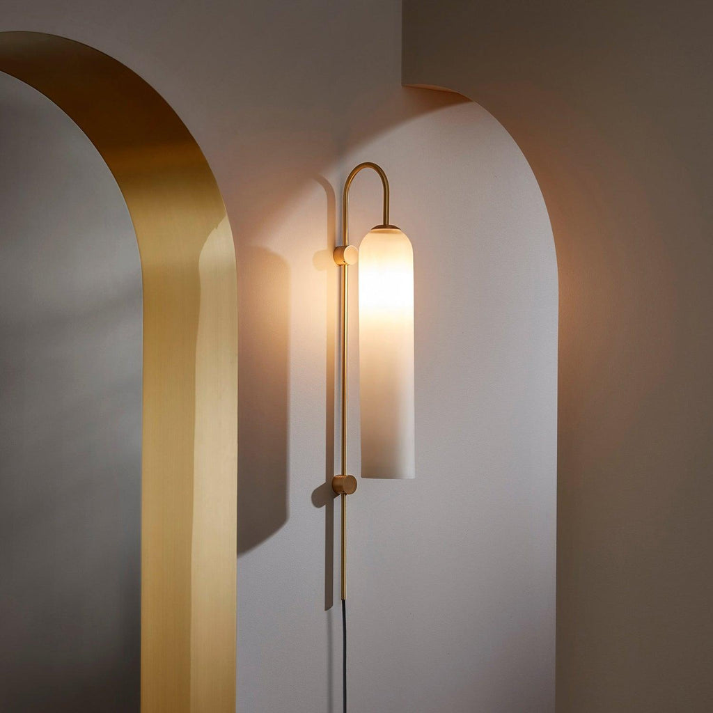 Clérachic mouth-blown glass wall sconce lighting a curved plaster alcove beside a brass arch, its frosted shade glowing warm.