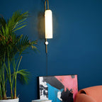 Clérachic mouth-blown glass wall sconce in opal white on a deep blue wall, lit above a palm and a leaning abstract canvas.