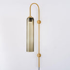 Clérachic mouth-blown glass wall sconce in olive-toned smoke glass on gold, dimly lit against an off-white wall.