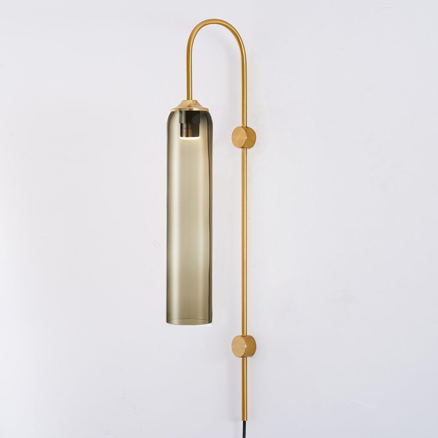 Clérachic mouth-blown glass wall sconce in olive-toned smoke glass on gold, dimly lit against an off-white wall.