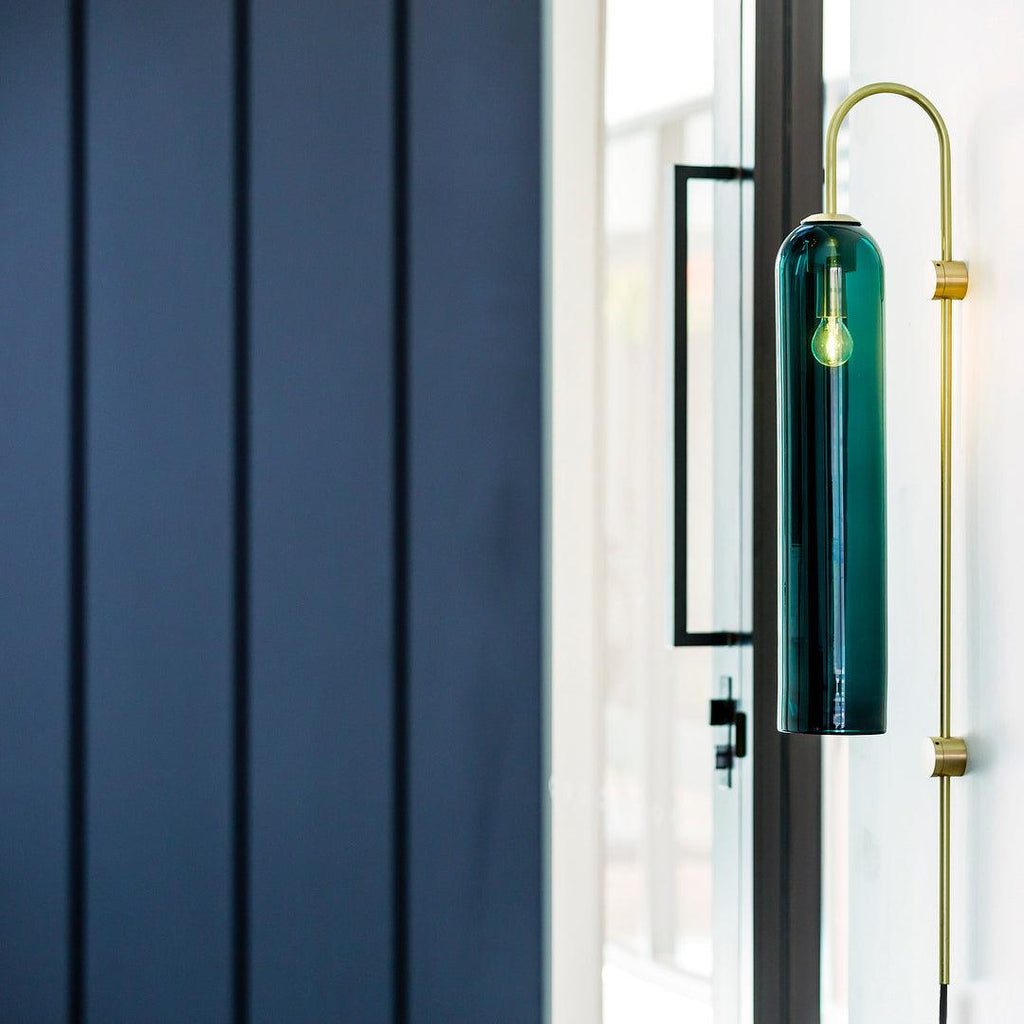 Clérachic mouth-blown glass wall sconce in teal beside a glazed door, lit, against navy timber panelling.