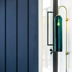 Clérachic mouth-blown glass wall sconce in teal beside a glazed door, lit, against navy timber panelling.
