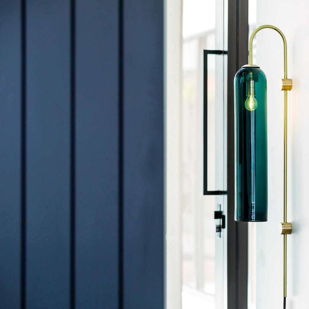 Clérachic mouth-blown glass wall sconce in teal beside a glazed door, lit, against navy timber panelling.