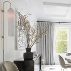 Clérachic mouth-blown glass wall sconce in frosted white in a dining room, beside blossom branches and grey curtains.