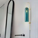 Clérachic mouth-blown glass wall sconce in teal above a bathroom tap, its filament bulb glowing behind blue glass.