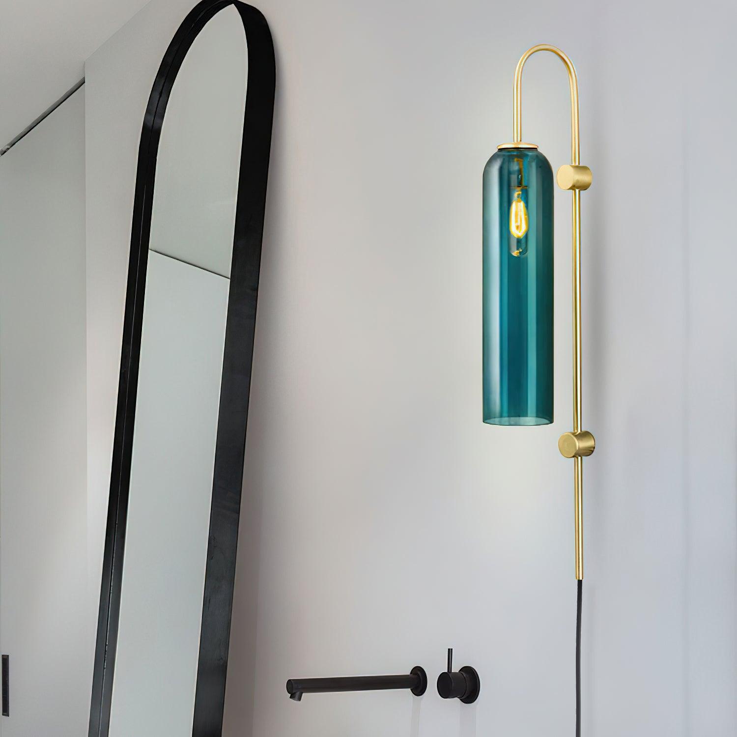 Clérachic mouth-blown glass wall sconce in teal above a bathroom tap, its filament bulb glowing behind blue glass.