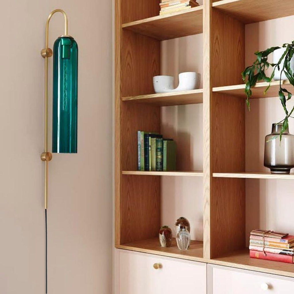 Clérachic mouth-blown glass wall sconce in emerald green on a blush wall, next to oak shelving full of books.