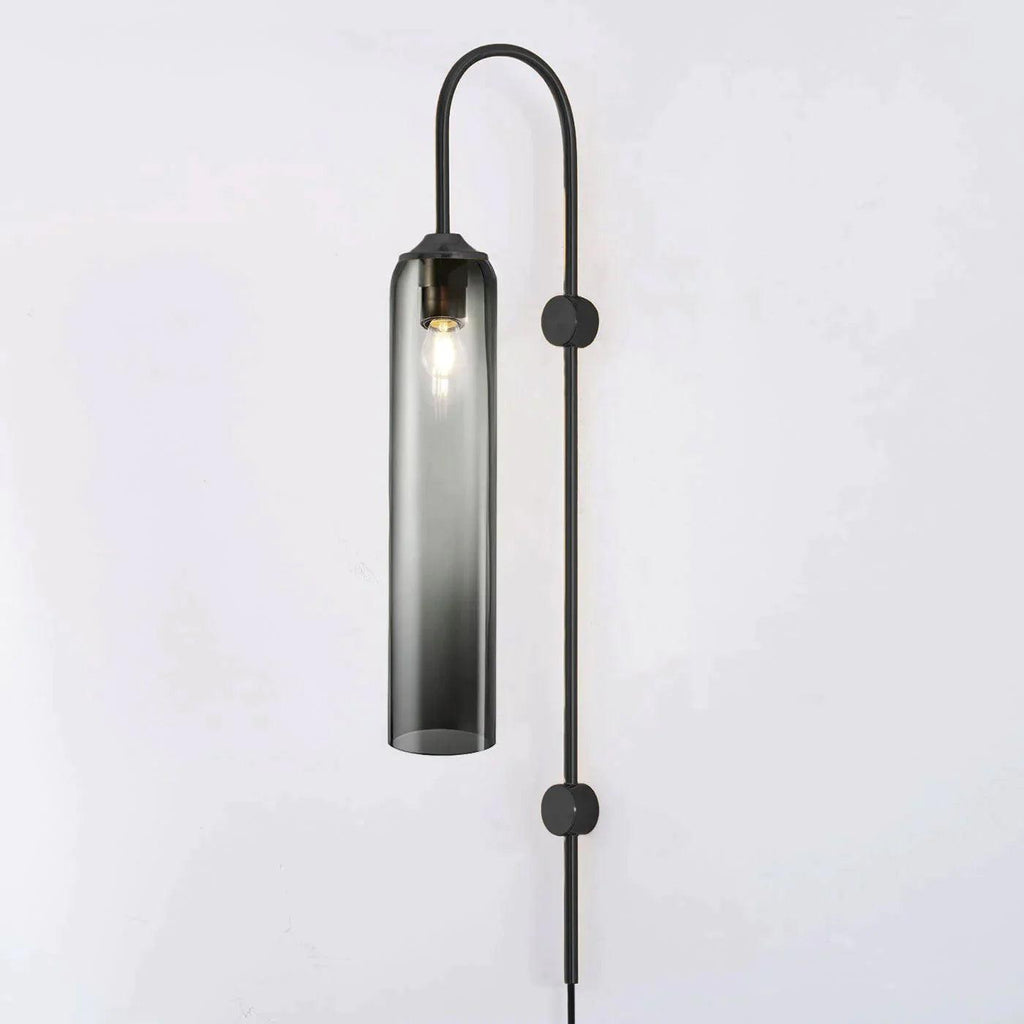 Clérachic mouth-blown glass wall sconce in smoke grey on black, lit, the bulb visible through the tinted glass.