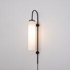 Clérachic mouth-blown glass wall sconce in opal white on black, lit brightly and washing the wall behind it warm.