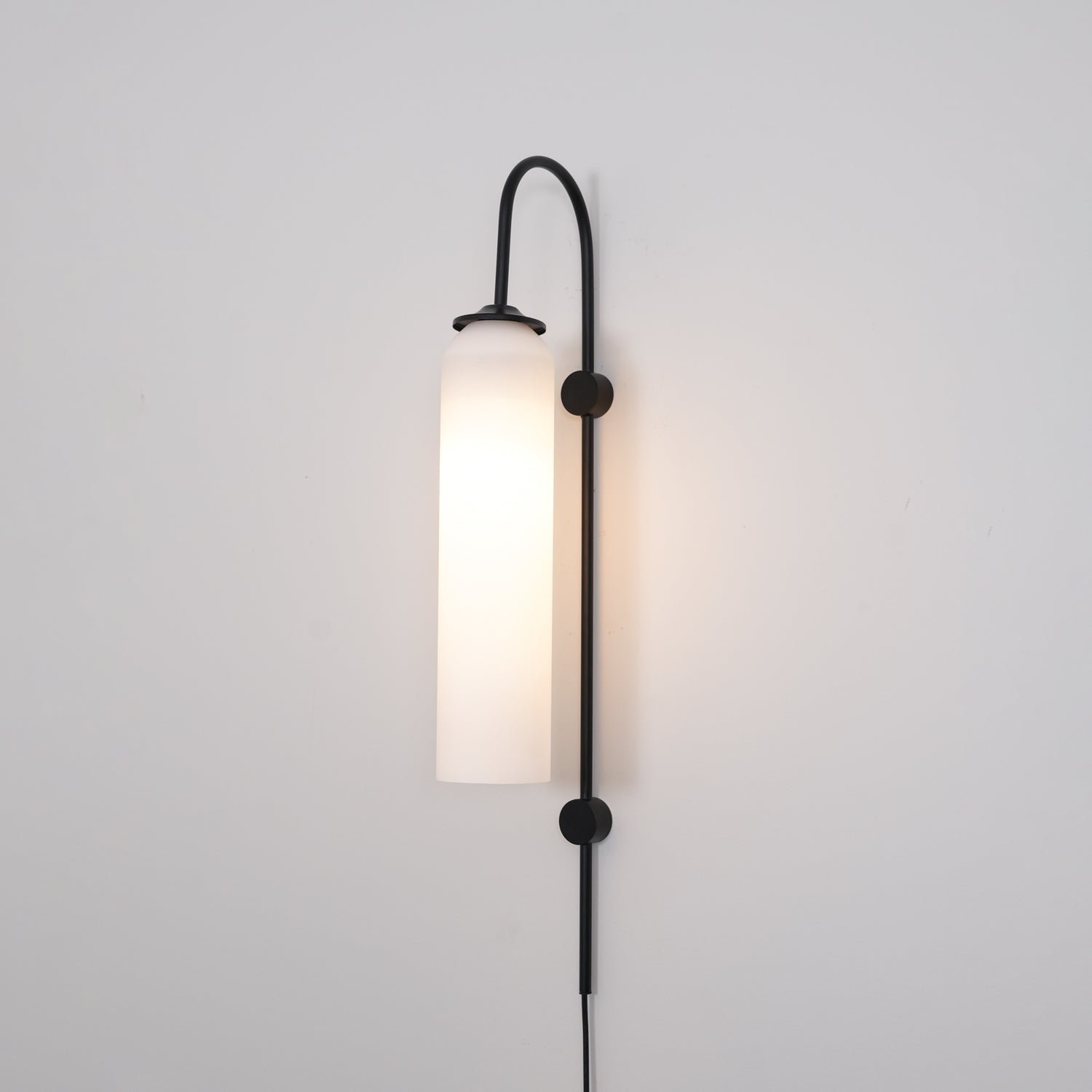 Clérachic mouth-blown glass wall sconce in opal white on black, lit brightly and washing the wall behind it warm.