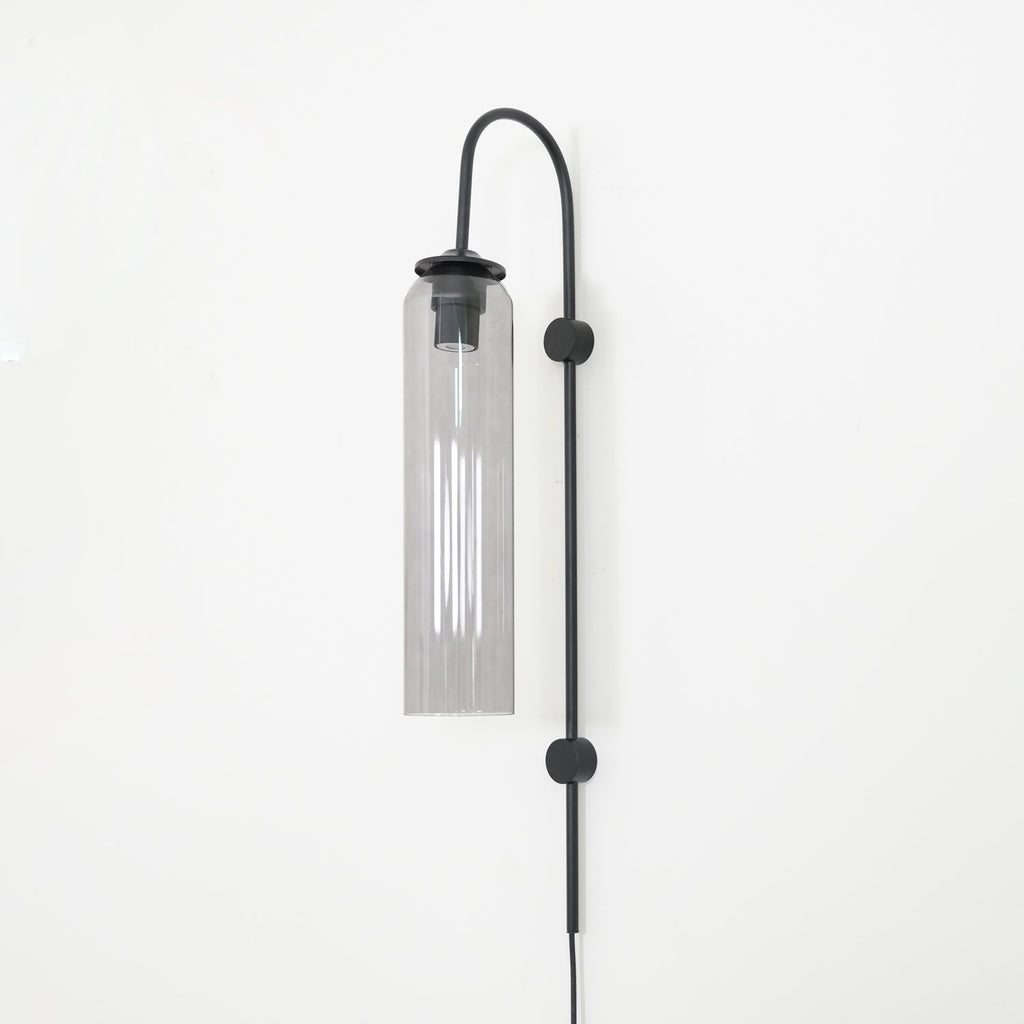 Clérachic mouth-blown glass wall sconce in smoke grey on black, unlit, the black cap and sleeve visible at the top.