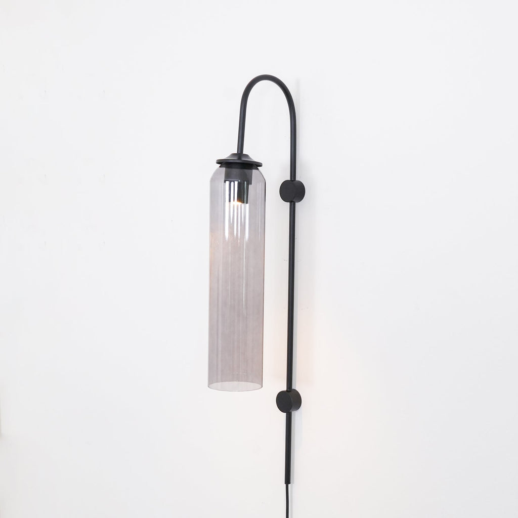 Clérachic mouth-blown glass wall sconce in smoke grey on black, dimly lit, the glass darkest at the shoulder.