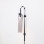 Clérachic mouth-blown glass wall sconce in smoke grey on black, dimly lit, the glass darkest at the shoulder.
