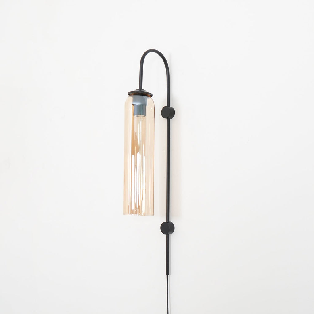 Clérachic mouth-blown glass wall sconce in amber on black, lit, with a long streak of light down the inside.