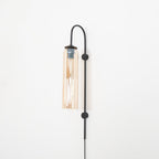 Clérachic mouth-blown glass wall sconce in amber on black, lit, with a long streak of light down the inside.