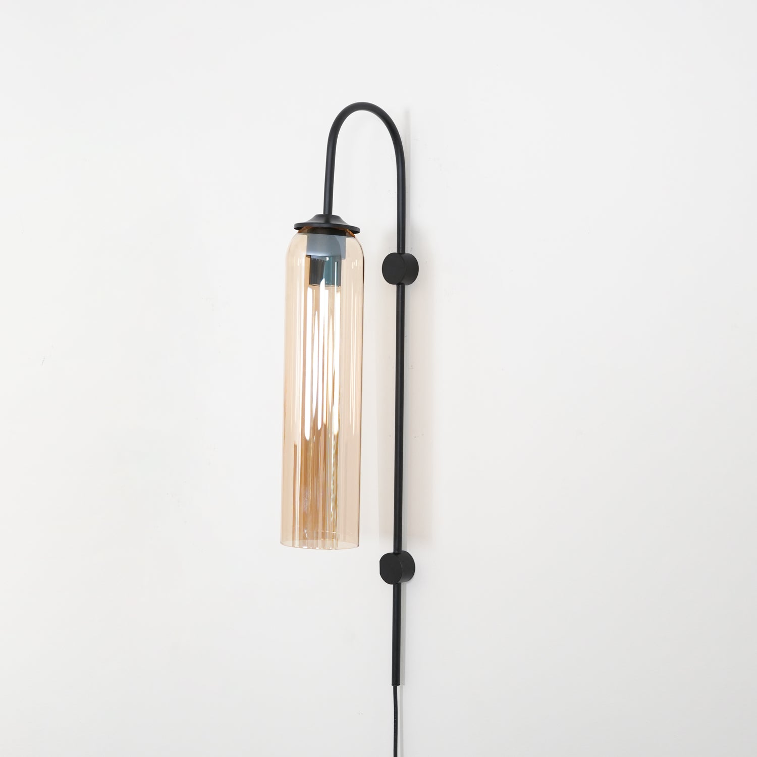 Clérachic mouth-blown glass wall sconce in amber on black, brightly lit, the whole cylinder turned honey gold.
