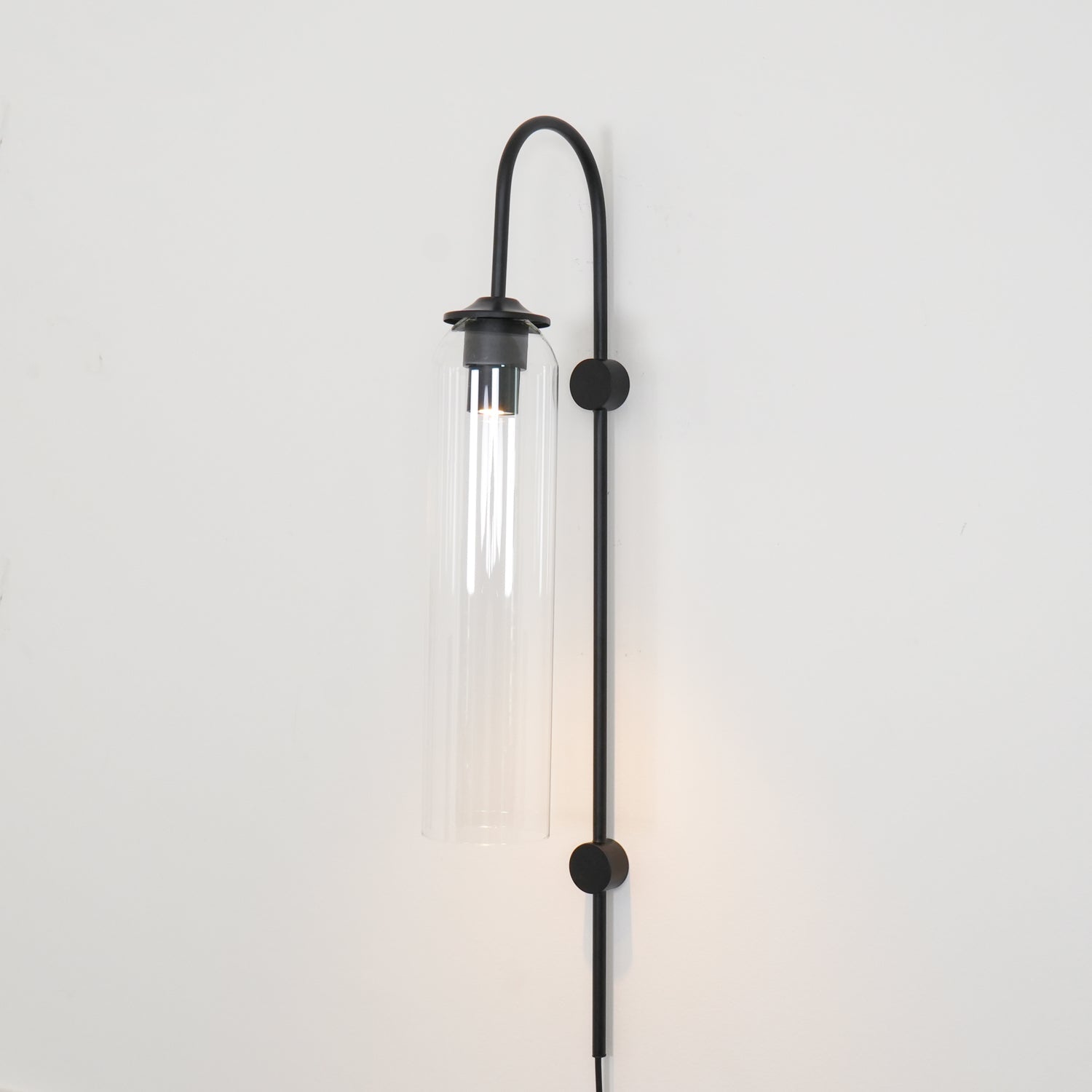 Clérachic mouth-blown glass wall sconce in clear glass on black, lit, light falling in a defined pool below the foot.