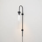 Clérachic mouth-blown glass wall sconce in clear glass on black, lit, with a warm wash spreading up the wall.