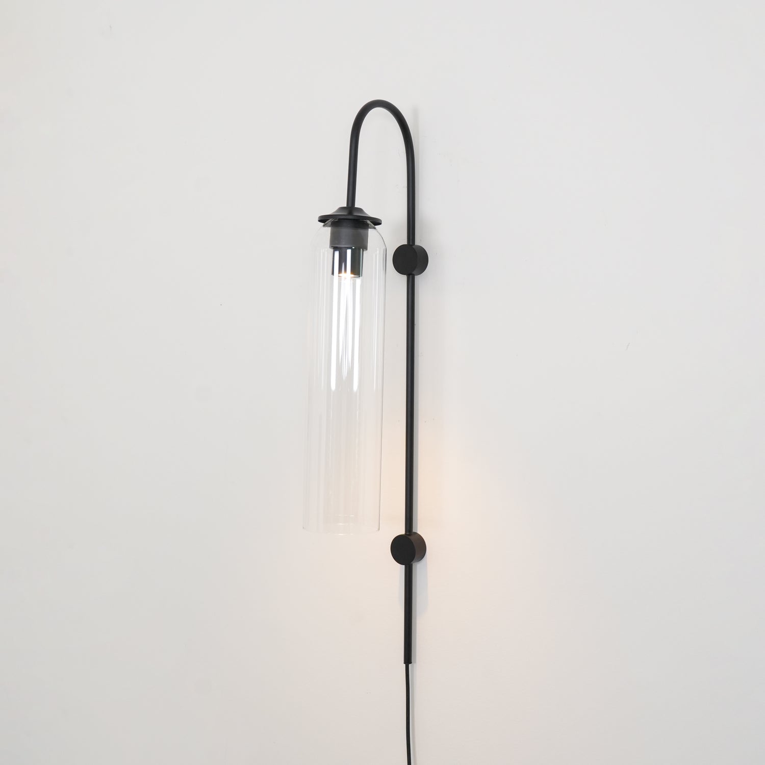 Clérachic mouth-blown glass wall sconce in clear glass on black, lit, with a warm wash spreading up the wall.