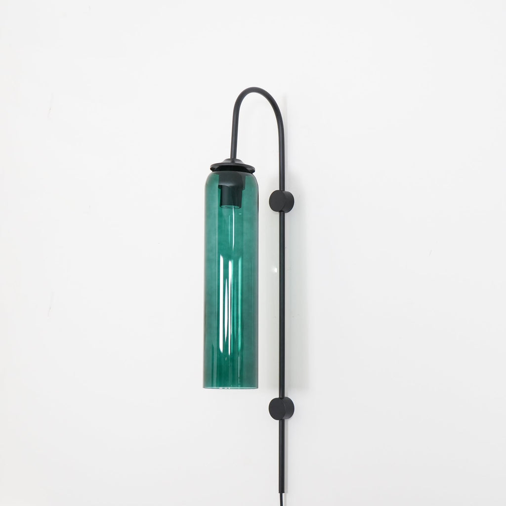 Clérachic mouth-blown glass wall sconce in green glass on black, unlit, hung from the curve of its gooseneck.