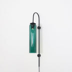 Clérachic mouth-blown glass wall sconce in green glass on black, lit, the colour lifting where the bulb sits.