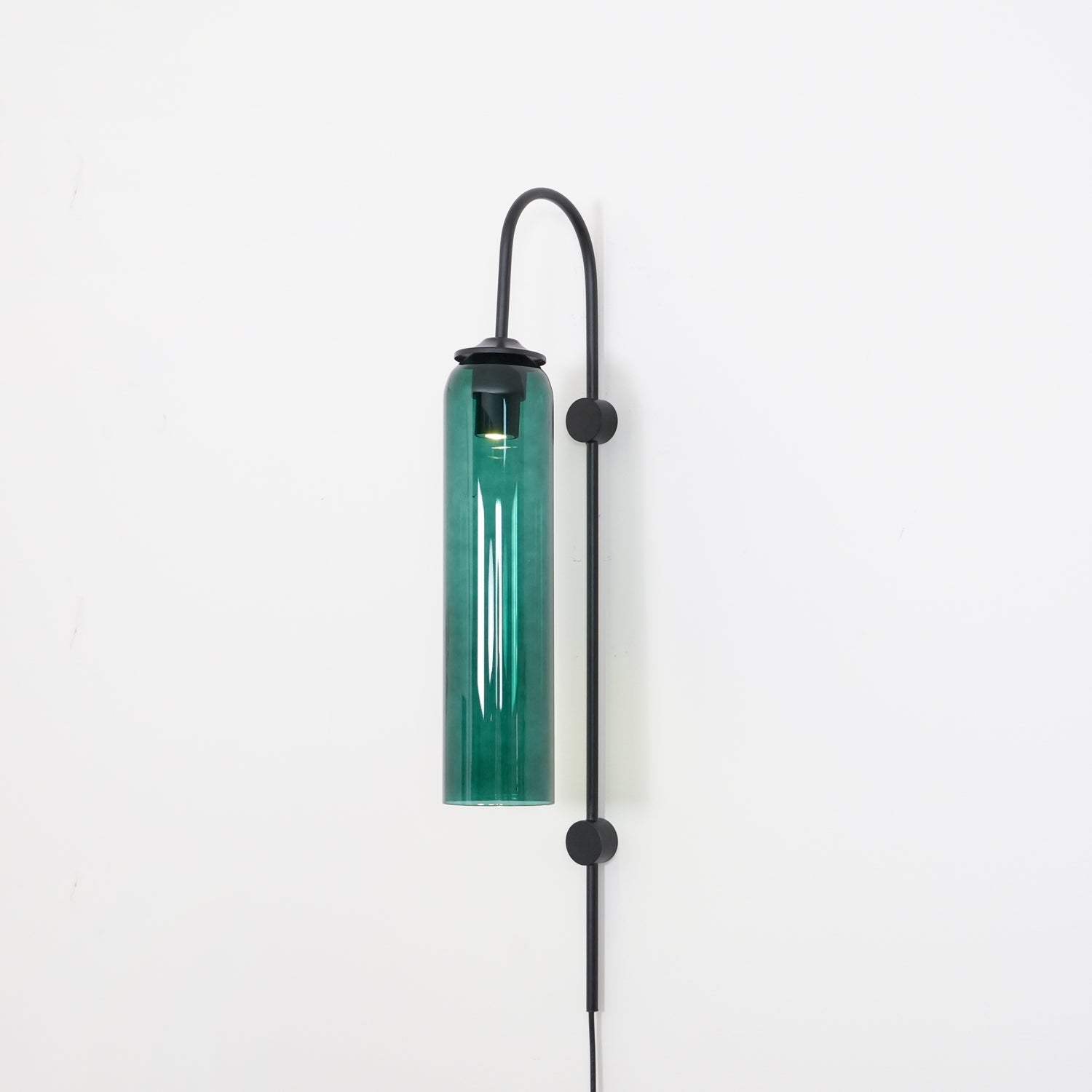 Clérachic mouth-blown glass wall sconce in green glass on black, lit, the colour lifting where the bulb sits.