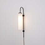 Clérachic mouth-blown glass wall sconce in frosted white on black, lit, the wall behind it turning warm.