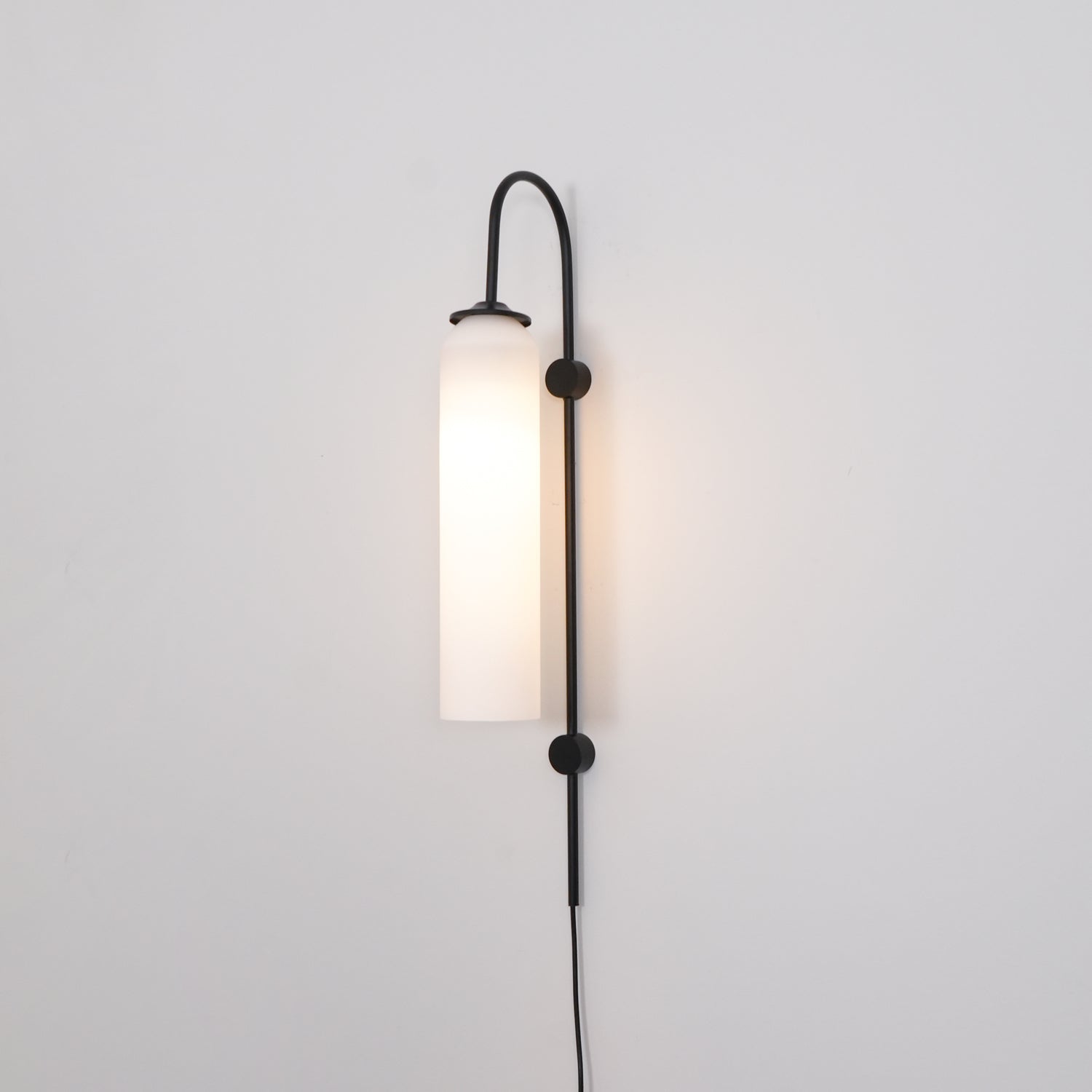 Clérachic mouth-blown glass wall sconce in frosted white on black, lit, the wall behind it turning warm.
