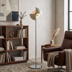 A Clérachic floor lamp in White & Chrome stands in a room of bookshelves and framed artwork, gloss shades inside a chrome ring.
