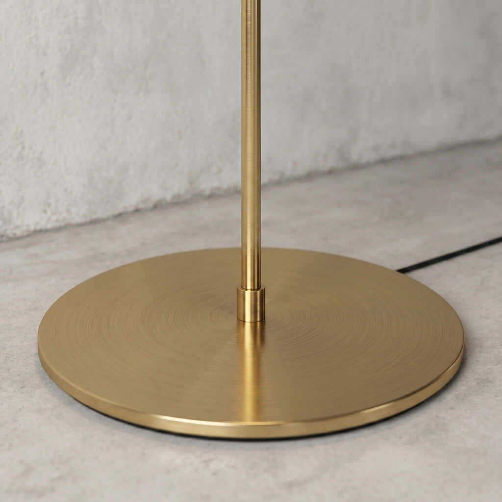Where the slim brushed brass stem meets the round weighted base of the Clérachic floor lamp, seen up close.
