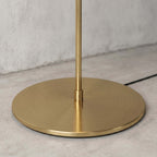 Where the slim brushed brass stem meets the round weighted base of the Clérachic floor lamp, seen up close.