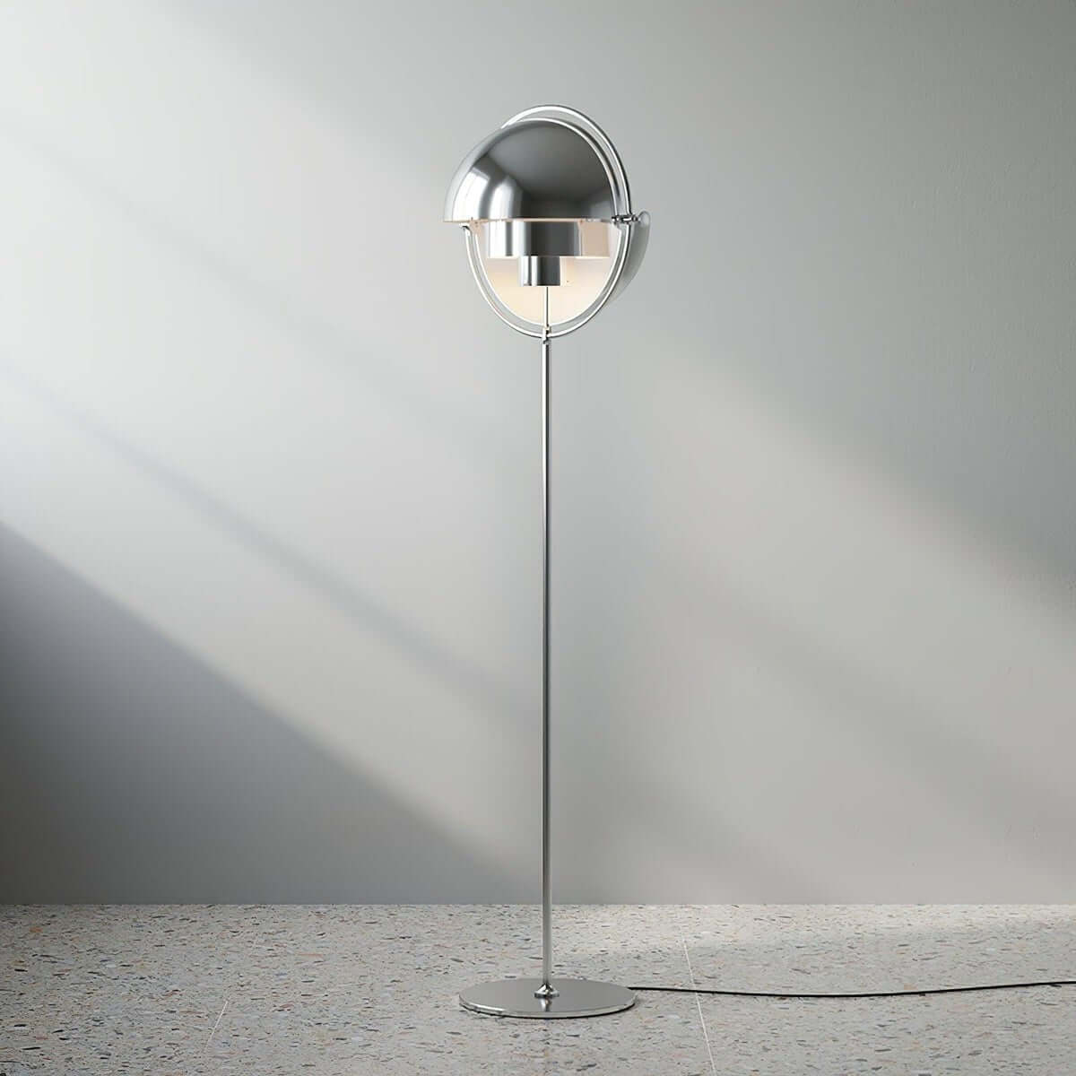 Casting a soft shadow on a pale wall, the lit Clérachic floor lamp in Chrome shows its polished shades and slim stem.