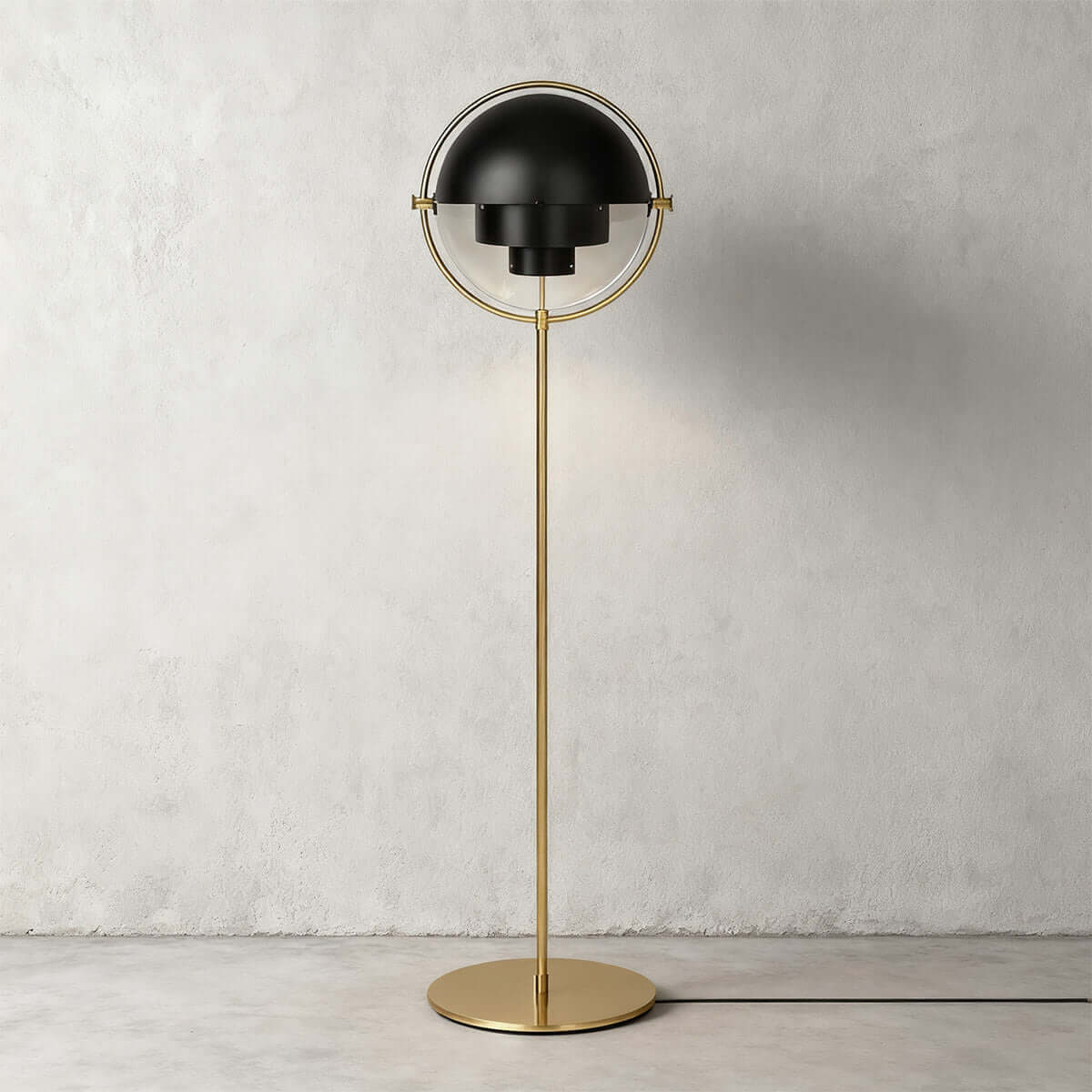 Matt black shades over a brushed brass frame: the Clérachic floor lamp in Black & Brass against pale concrete.