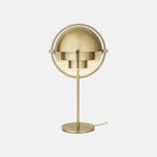 The Clérachic table lamp in Brass, brushed across shades, ring, stem and base, with its textile mains cord trailing from the round base.