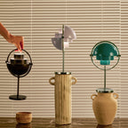 Three Clérachic lamps in dark bronze, lilac and deep green, one lifted by its ring handle to show how it carries.