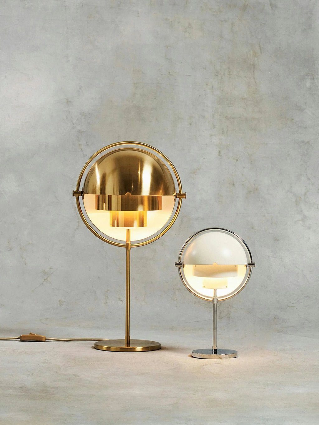 The Clérachic rechargeable lamp in white and chrome lit beside the taller corded model, shown for scale against a concrete wall.