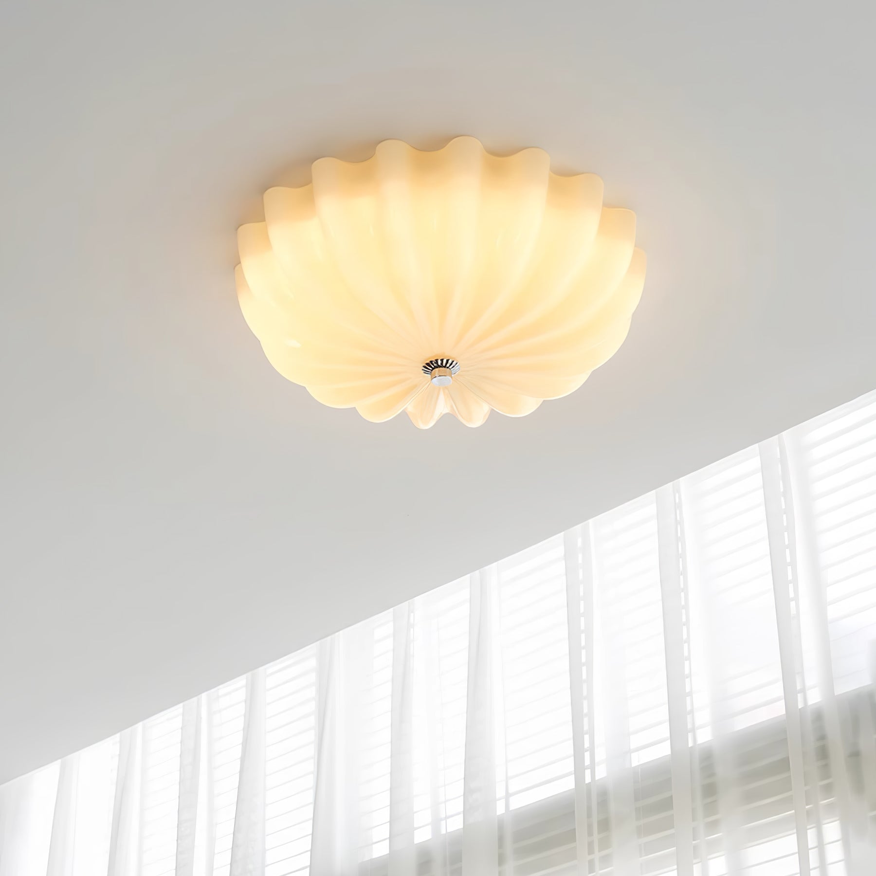 Clérachic Murano-Style Scalloped Glass Flush Ceiling Light in beige, lit warm on a white ceiling beside a tall sheer-curtained window.